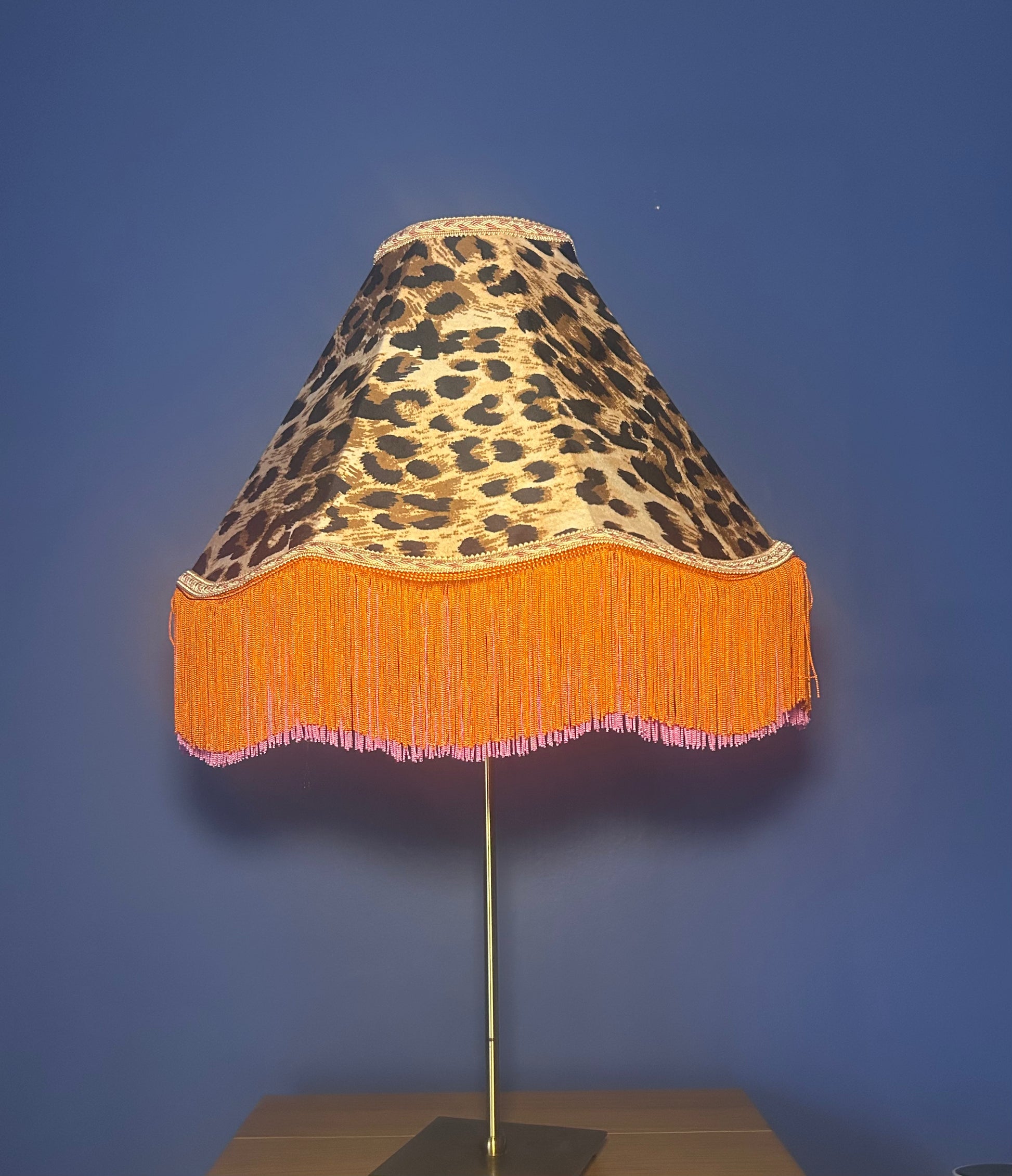 Lamp with leopard print shade and orange fringe on a blue background